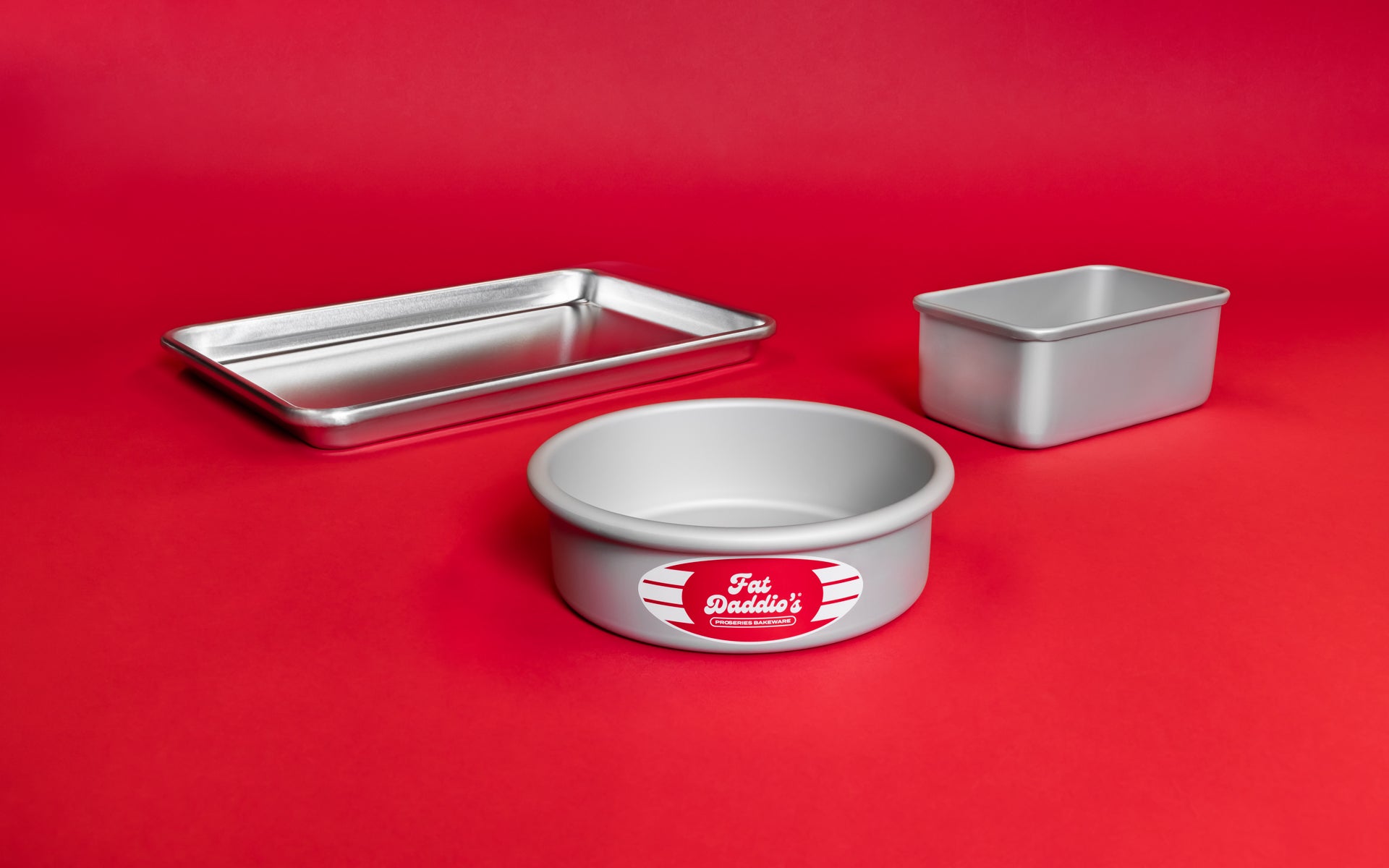 A baking sheet pan, round cake pan and bread pan on a bold red background