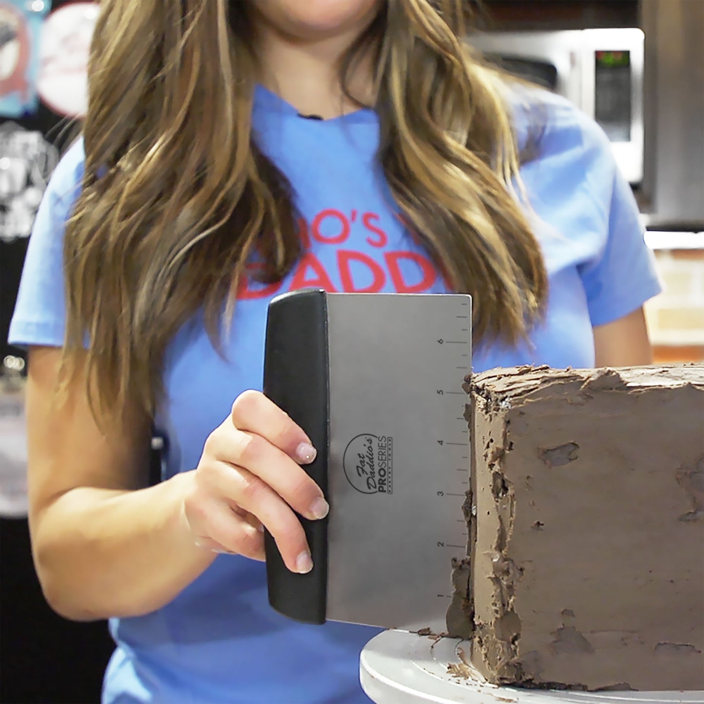 Meisha Tate using a bench scraper used for shaping smoothing ganache on a chocolate square cake