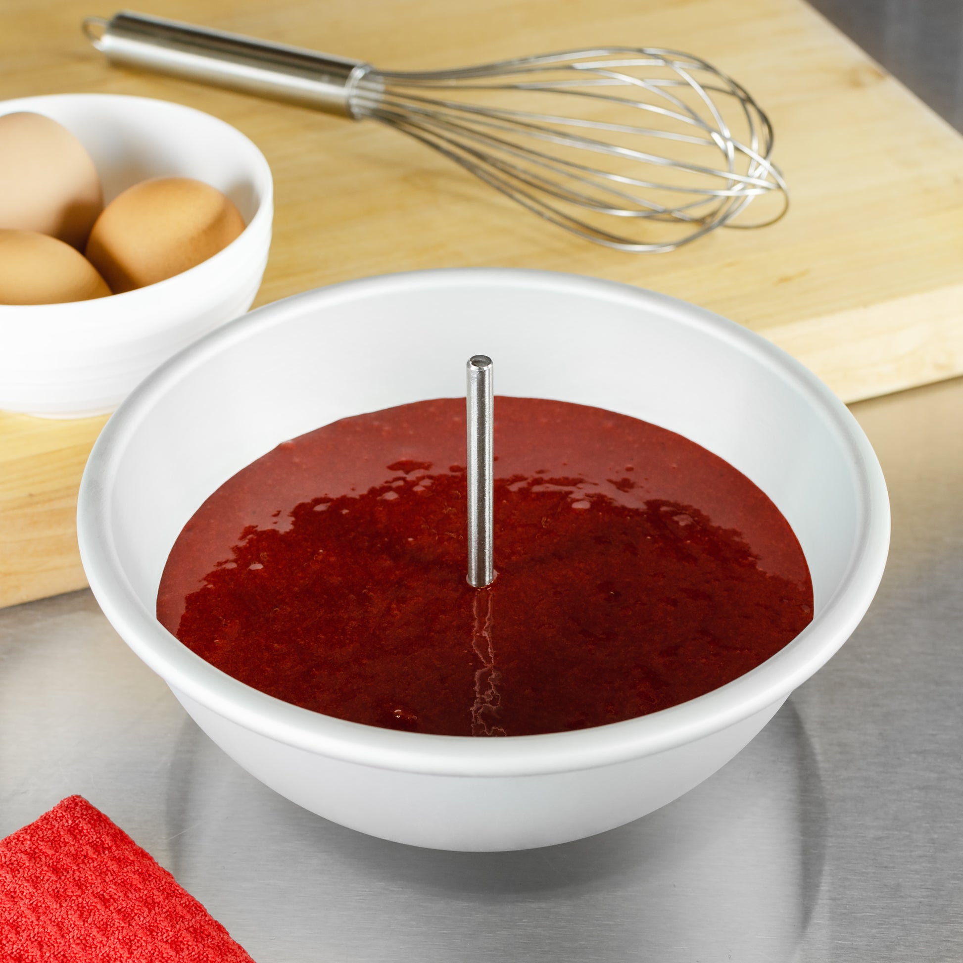 Heating Core Rod submerged in red velvet in a hemisphere cake pan with cutting board, eggs and tools in a bakery