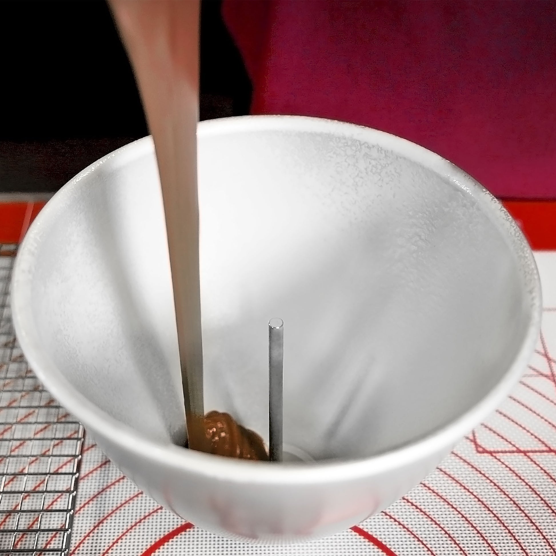 Heating core rod in a doll cake pan with batter being poured around it by a baker