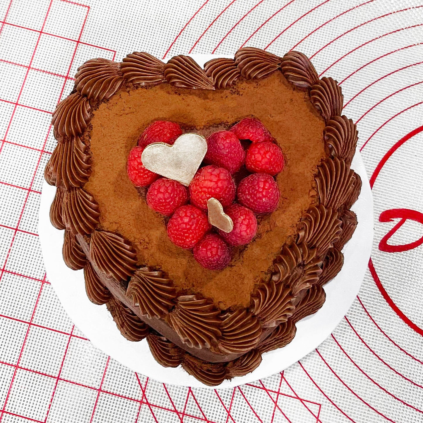 Chocolate heart cake with raspberries on a work mat in a bakery