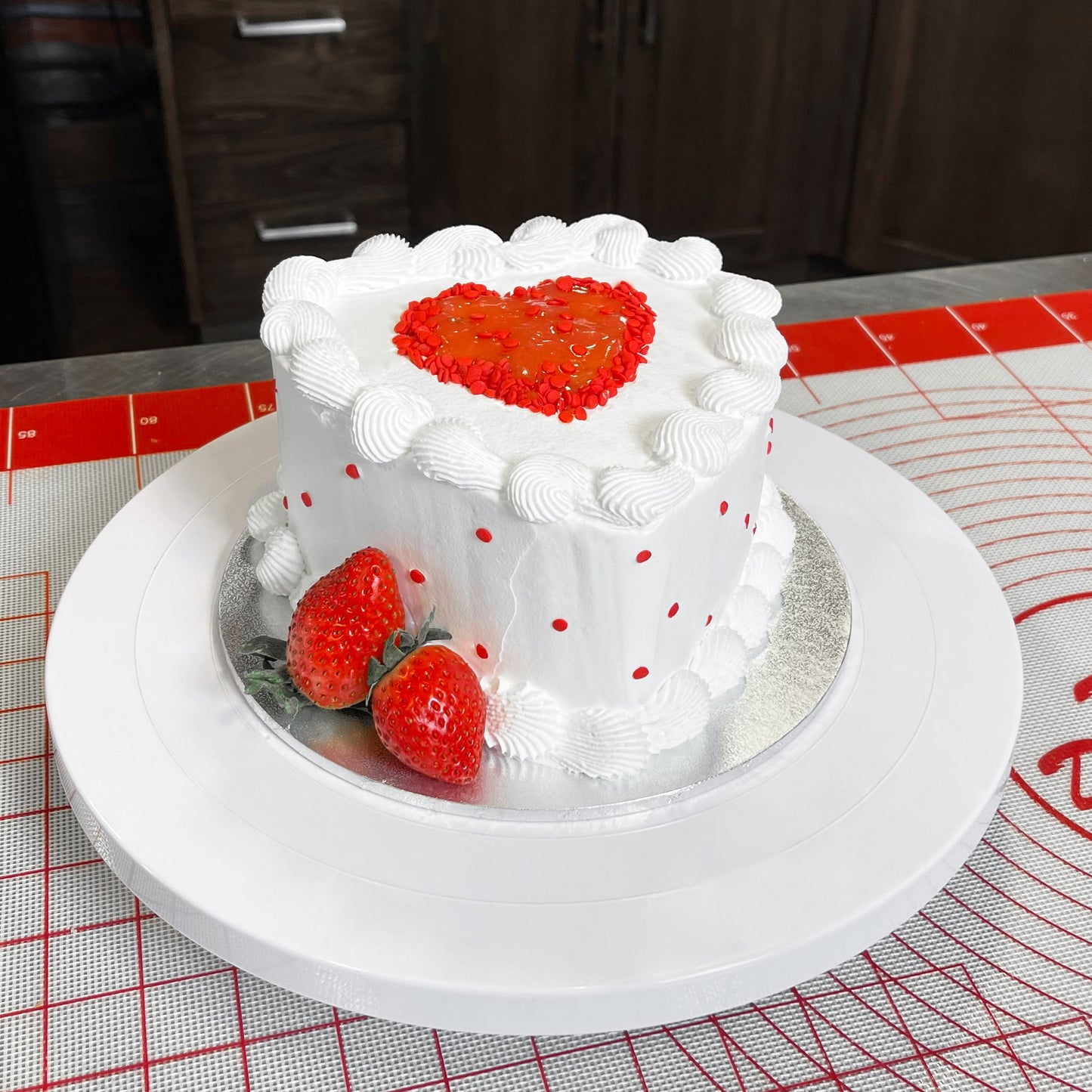 Decorated white heart cake with strawberries on a silicone work mat