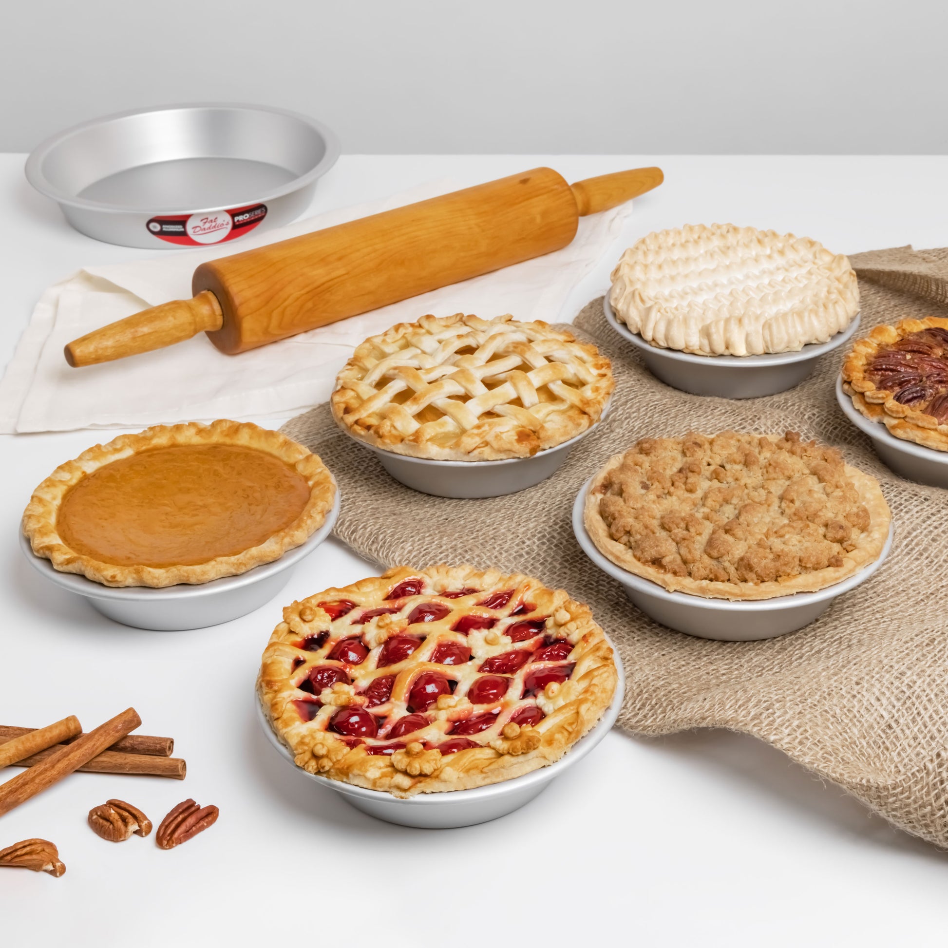 Assortment of fall pies on burlap with cinnamon sticks, walnuts, wooden rolling pin on linen in a home kitchen