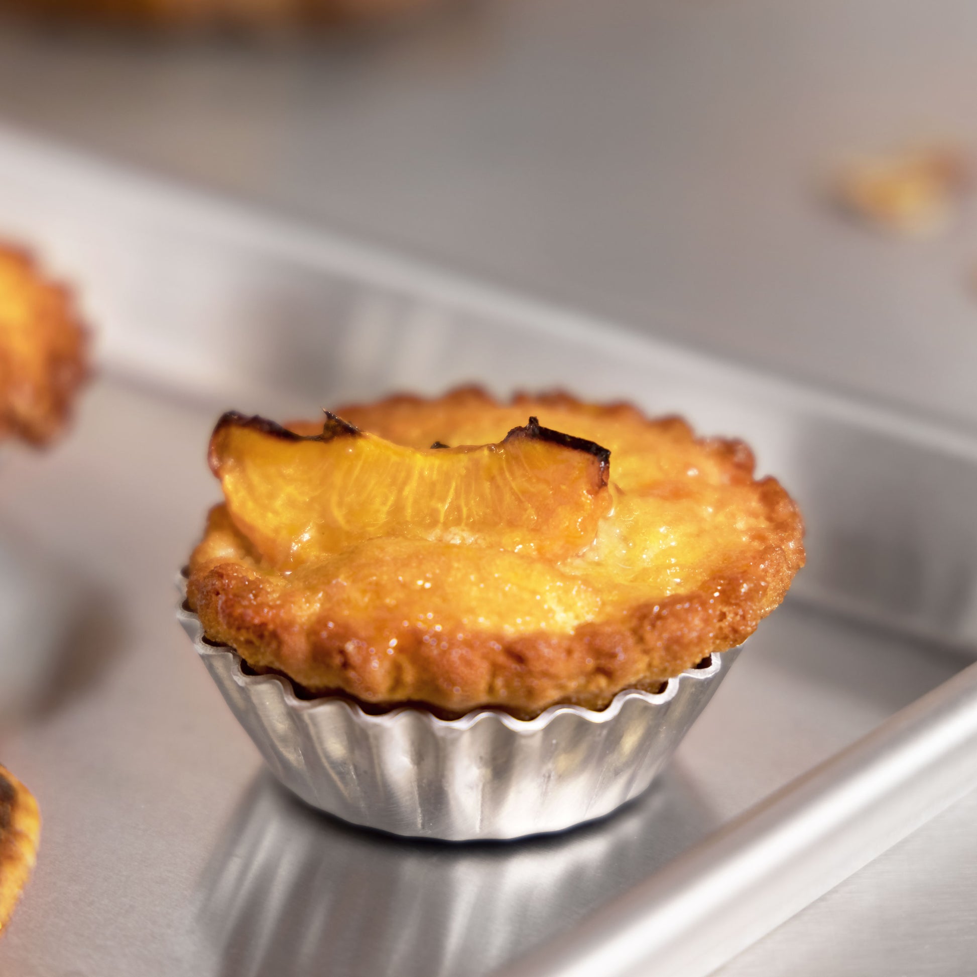 Peach mini tartlette in a pan sitting on a sheet pan in a commercial kitchen