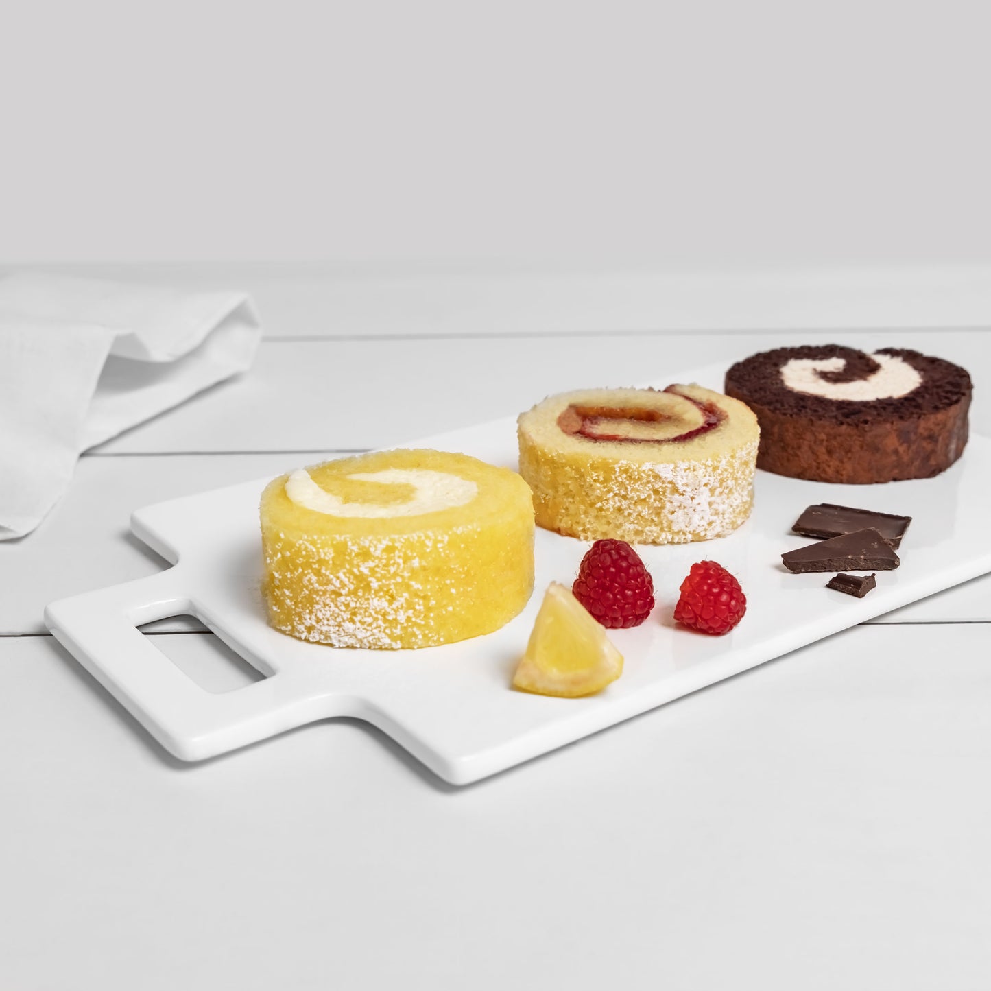 Yellow, spice and chocolate Jelly Roll slices plated on a serving dish with fruit and chocolate garnishes in a home kitchen