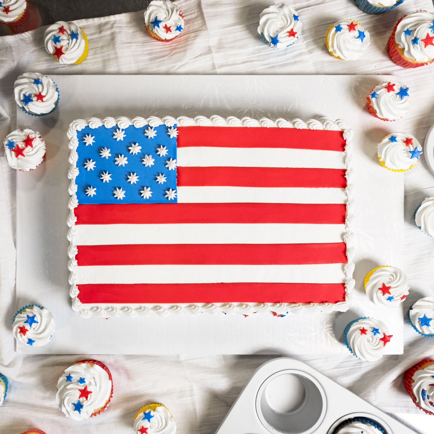 An decorated American flag sheet cake with patriotic cupcakes and a standard muffin pan in a home kitchen