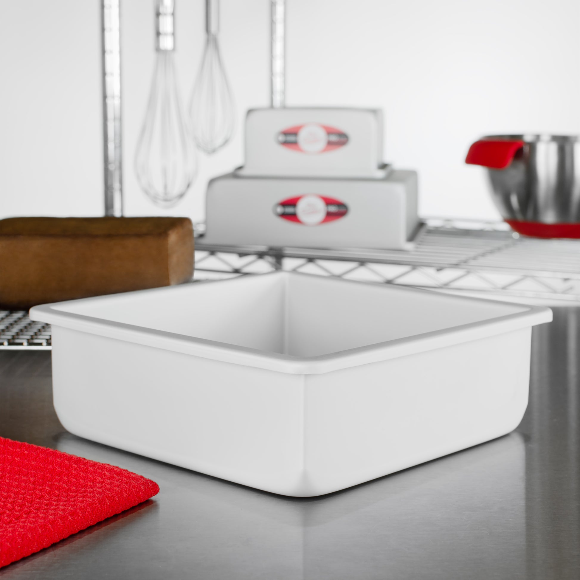 Square cake pans with chocolate cake, tools, and bowls in a bakery