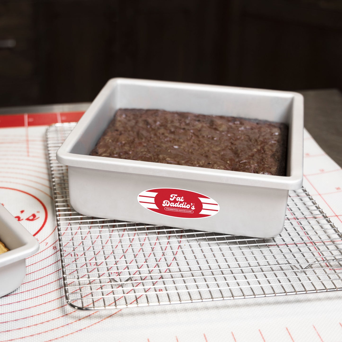 Removable bottom square cheesecake pan pan 9 x 9 x 3 with a brownie on a cooling rack and work mat in a bakery