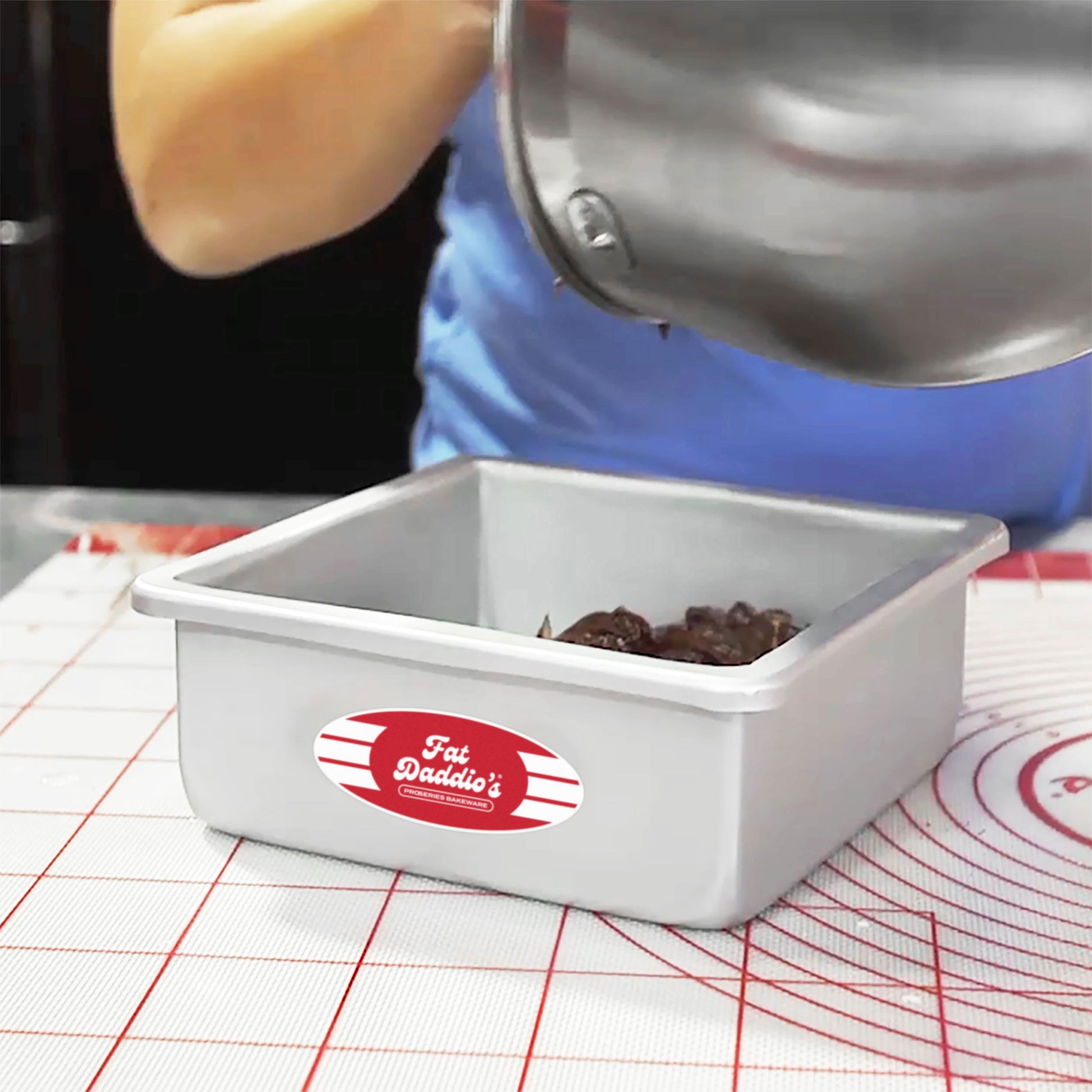 Miesha Tate scooping chocolate batter into a square cake pan on a work mat in a bakery