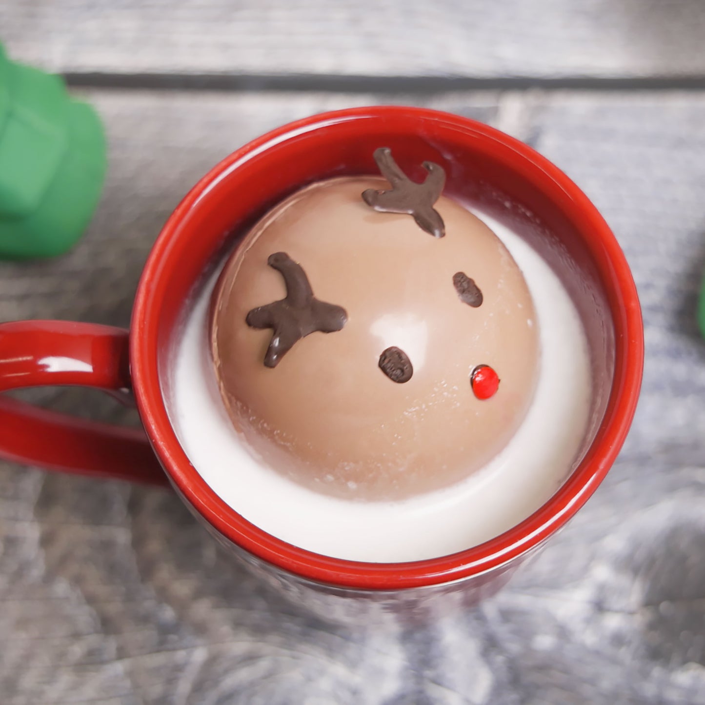 A reindeer chocolate bomb in hot cocoa with a red mug in a home kitchen