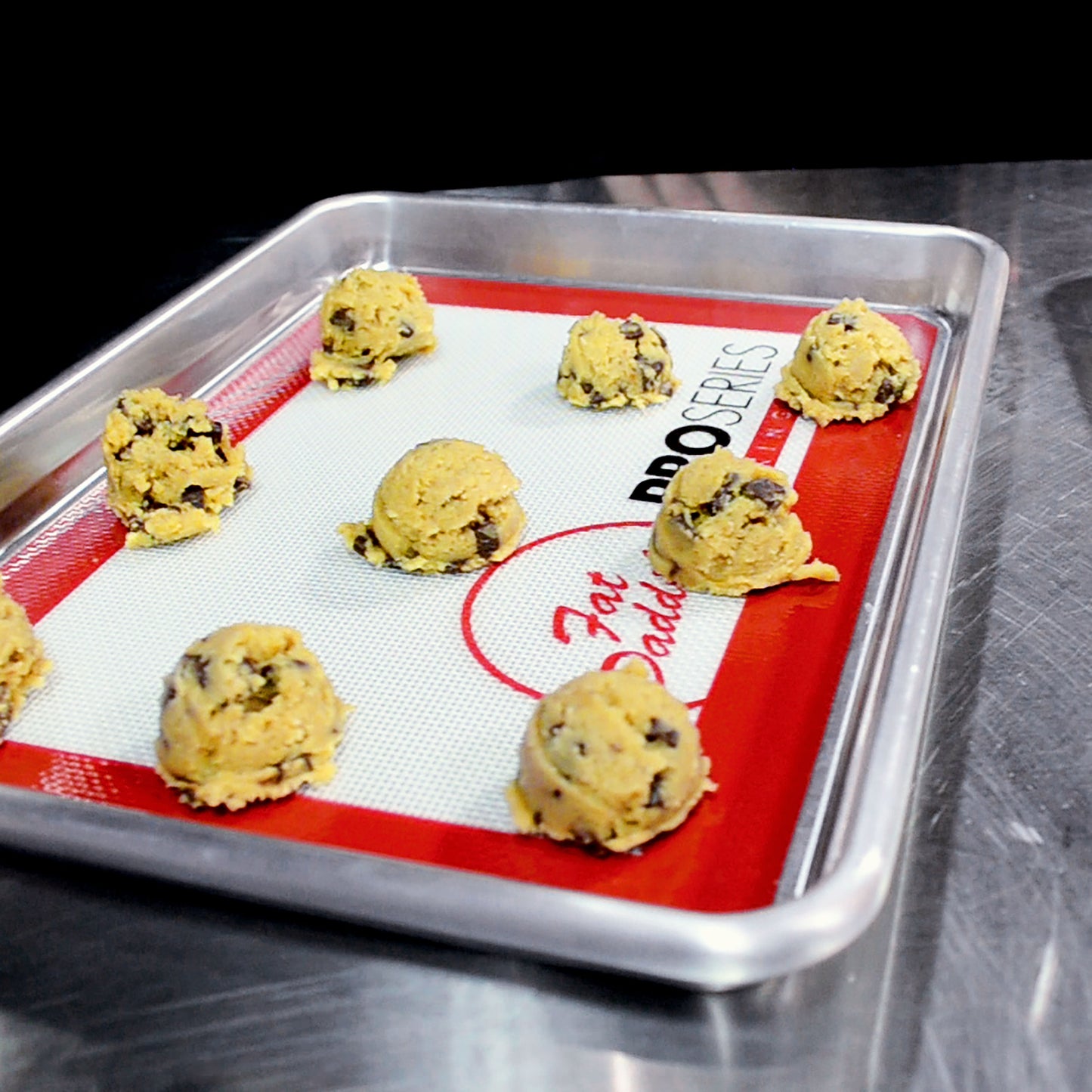 Chocolate chip cookie dough scoops on baking mats nested in a baking sheet pan in a commercial kitchen