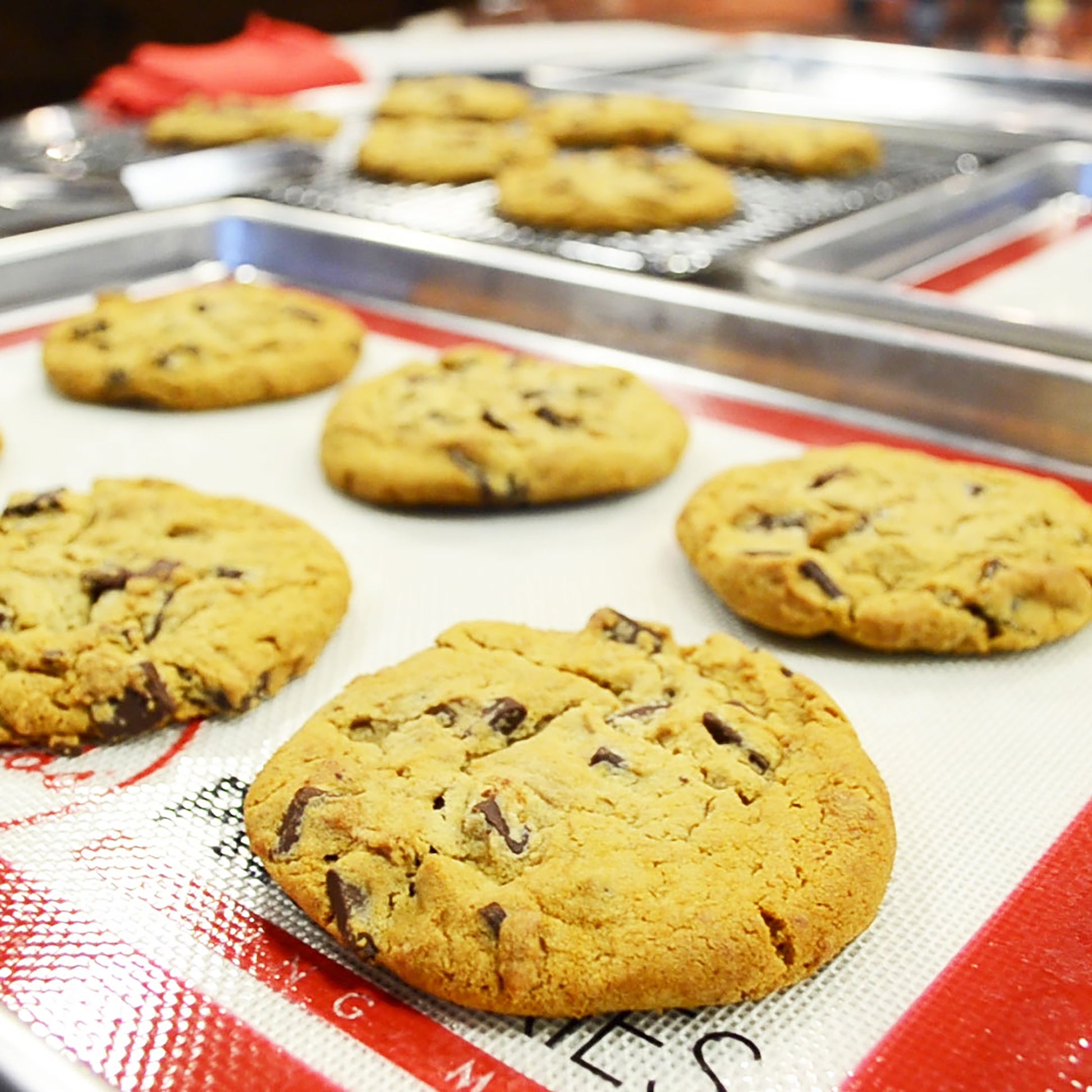 Chocolate chip cookies on baking mats nested in a baking sheet pan in a commercial kitchen