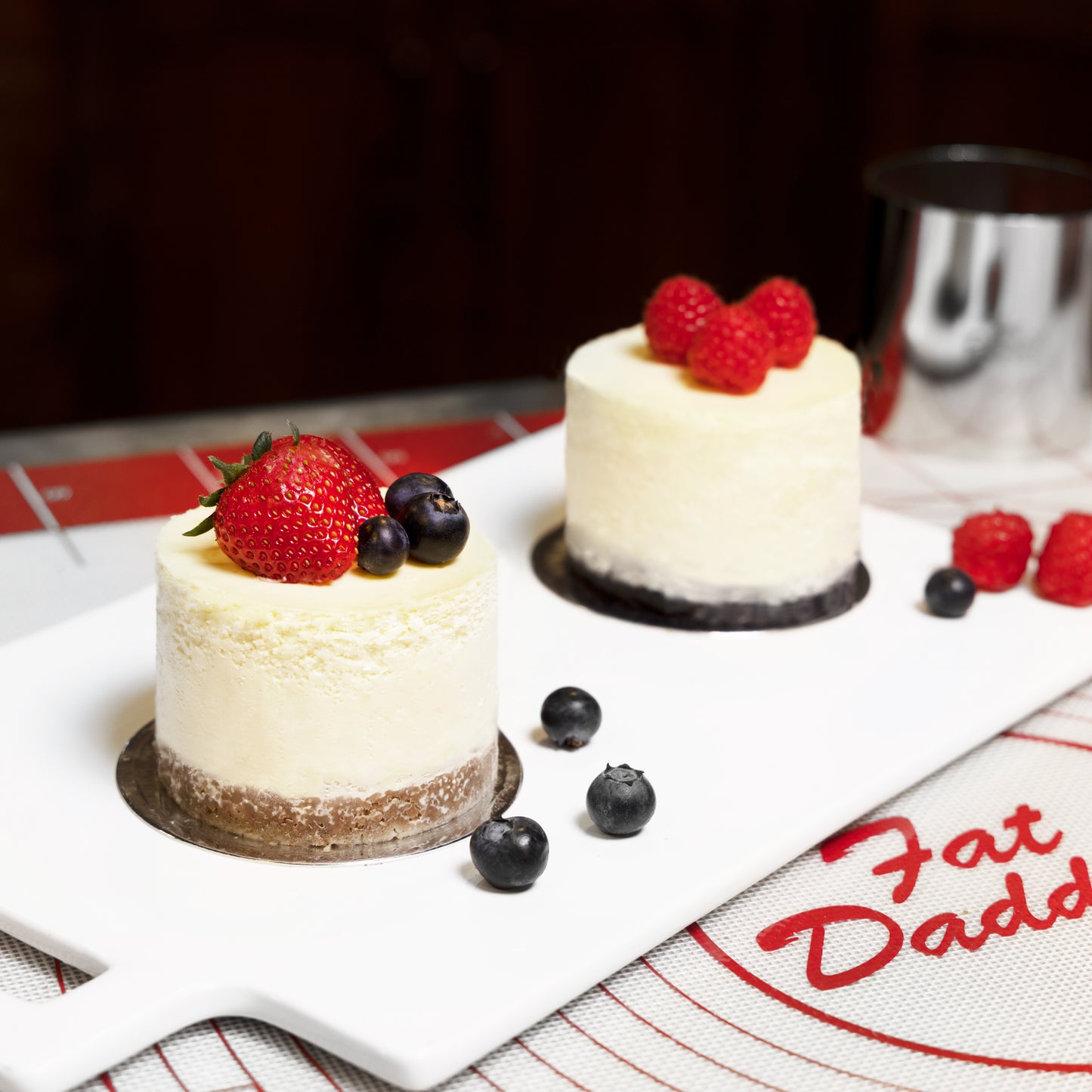 Two small round cheesecakes with strawberries and blueberries served on a silicone work mat